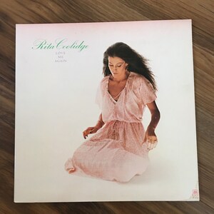 May include: A vintage vinyl record album cover featuring Rita Coolidge. The cover is white with a pink background and features a photo of Rita Coolidge wearing a pink dress. The album title is "Love Me Again" and is printed in green text.