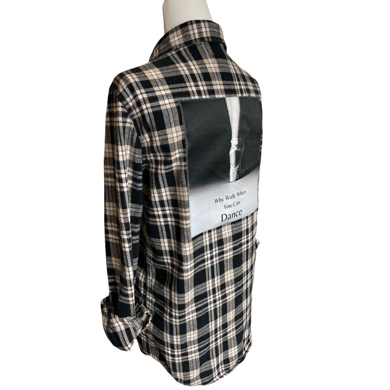 May include: Black and white plaid flannel shirt with a patch on the back that says "Why Walk When You Can Dance" and features a black and white photo of a dancer's leg in a pointe shoe.