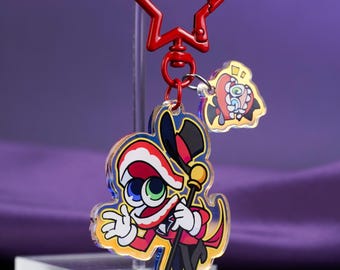 May include: An acrylic keychain featuring a cartoon character wearing a top hat and red coat, holding a cane. The charm is attached to a red star-shaped clasp and includes a smaller secondary charm depicting a stylized eye with red wings.