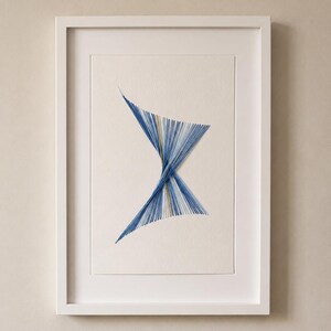 May include: A framed wall art piece featuring a geometric string art design on a cream-colored background. The artwork consists of multiple blue and white threads arranged in a twisted hourglass shape, creating a sharp, intersecting pattern.