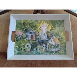 May include: A rectangular white serving tray with cutout handles featuring a watercolor illustration of four birdhouses nestled in a lush green garden setting with a small blue bird perched on one of the structures and soft yellow light.