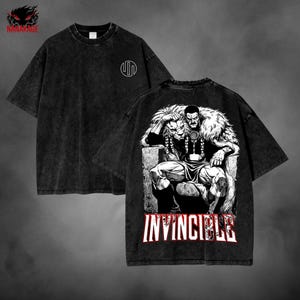 May include: Black t-shirt with a graphic on the back featuring a seated figure with a lion's head and the word "INVINCIBLE" in red and white. The front of the shirt has a white circular design. The brand name "NANAKAGE" is visible in the upper left corner.