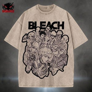 May include: Beige t-shirt with a black and white graphic of anime characters and the word "BLEACH". The shirt has a crew neck and short sleeves. The brand logo "NANAKAGE" is in the upper left corner.