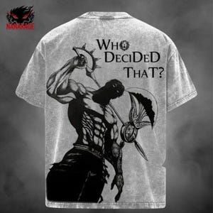 May include: Gray t-shirt with a graphic of a muscular figure wielding weapons, with the text "WHO DECIDED THAT?". The shirt also features the "NANAKAGE" logo in the upper left corner.