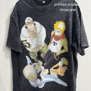 May include: Black graphic t-shirt with anime characters in different poses. The shirt has a vintage wash effect and the text "printed product showcase". The characters are in shades of white, orange, yellow, and blue.