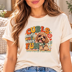 Puede incluir: Una camiseta color crema con un gráfico de un perro marrón de pelo rizado que lleva gafas en forma de corazón y un pañuelo floral verde. El texto dice "CURLS JUST WANNA HAVE FUN", "COCKAPOO VIBES", "HAPPIER PEOPLE FLUFFIER LIVES" y "GOOD DOGS GOOD TIMES ALWAYS TOGETHER."