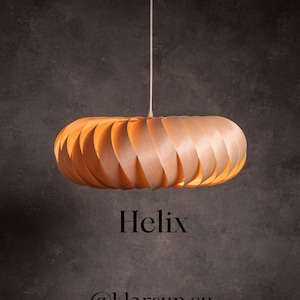 Puede incluir: Una lámpara colgante de madera con un diseño en espiral. La luz está hecha de finas láminas de madera curvadas, creando un efecto en capas. La palabra "Helix" está impresa debajo.