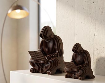 Puede incluir: Dos esculturas de madera marrón de una persona leyendo, con un diseño en capas. Las esculturas están sobre una estantería blanca, con una moderna lámpara de arco en el fondo. Las figuras están sentadas, concentradas en sus libros.