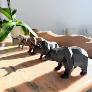 Four faceted animal statues, including a black bear and bull, are lined up on a marble surface with a plant and couch in the background.