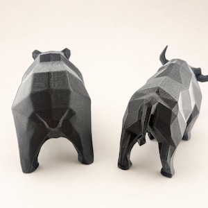 The backs of a black faceted bear and bull statue are shown on a light beige background.