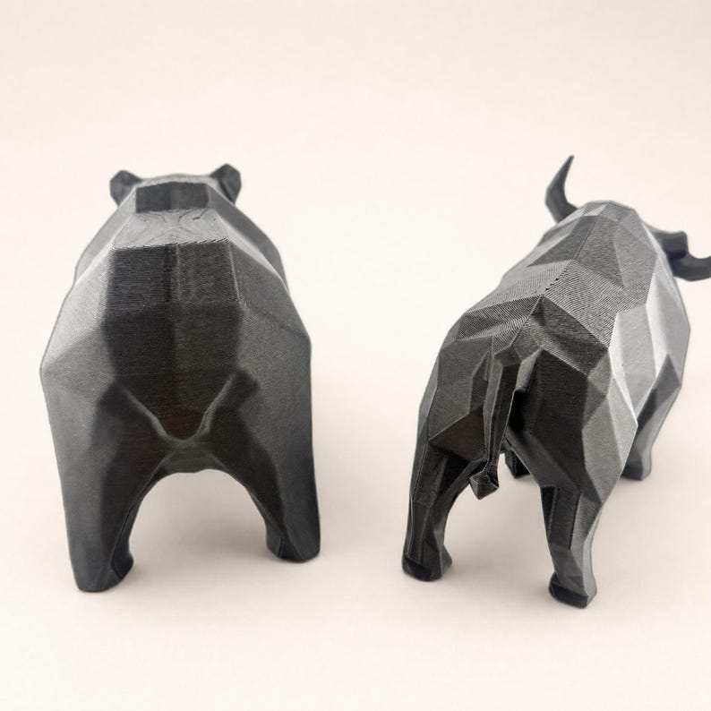 The backs of a black faceted bear and bull statue are shown on a light beige background.