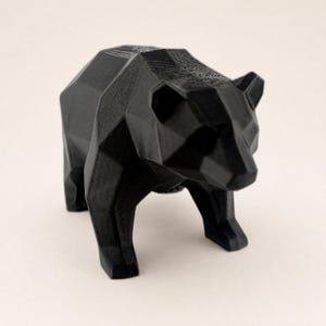 A black faceted bear statue is shown from a slightly elevated angle on a light beige background.