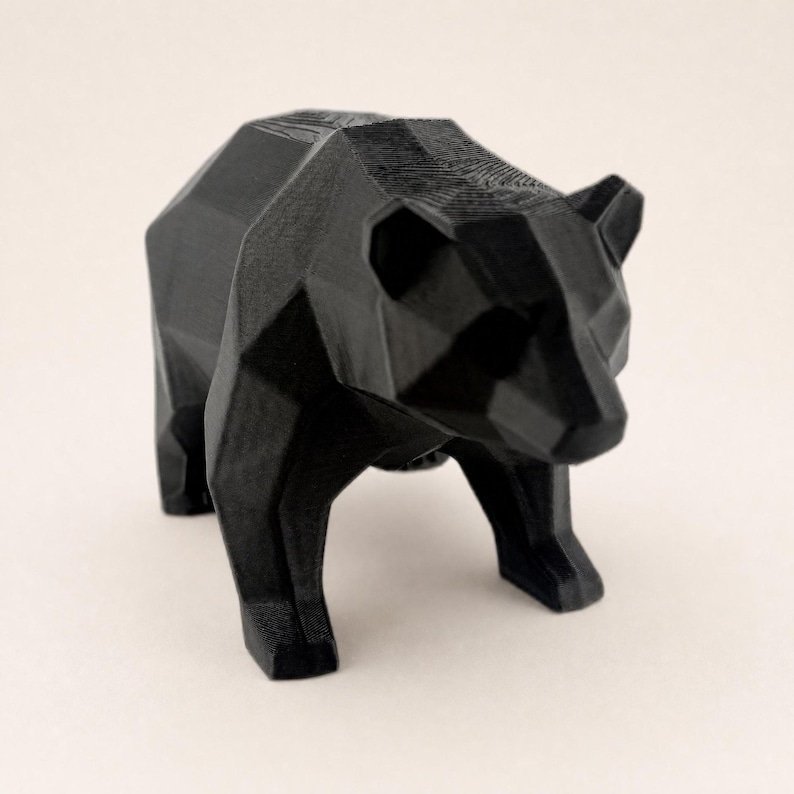 A black faceted bear statue is shown from a slightly elevated angle on a light beige background.