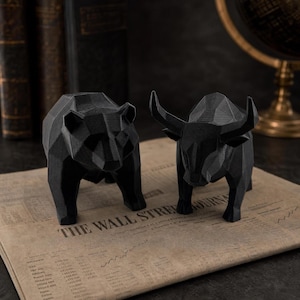 A black geometric bear and a black geometric bull statue are placed on an open newspaper with the headline "WALL STREET JOURNAL."