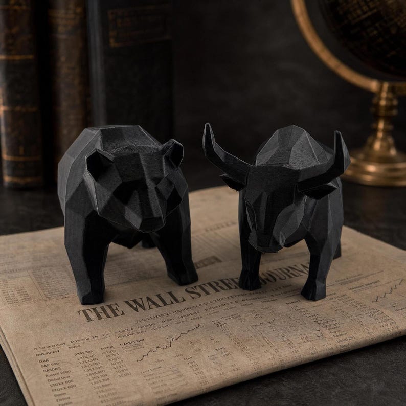 A black geometric bear and a black geometric bull statue are placed on an open newspaper with the headline "WALL STREET JOURNAL."
