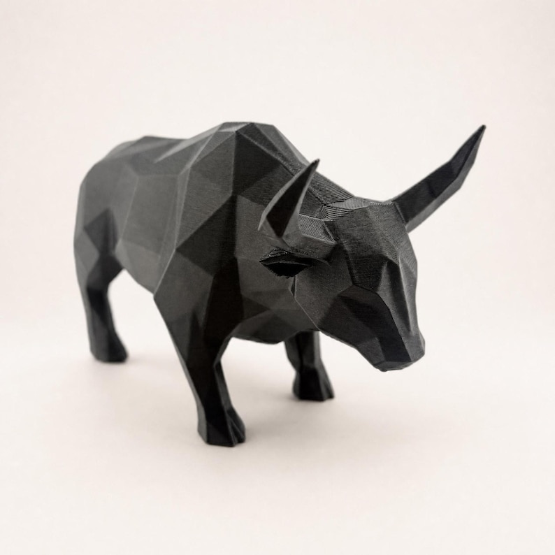 A black faceted bull statue is shown from a slightly elevated angle on a light beige background.