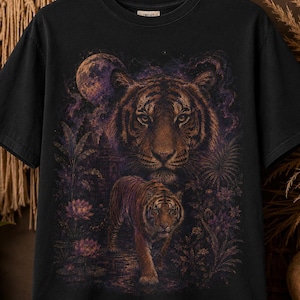 May include: A black short-sleeve t-shirt featuring a graphic print of a large tiger face above a smaller tiger walking through a jungle landscape with lotus flowers and a full moon in shades of purple, orange, and brown on the front chest.