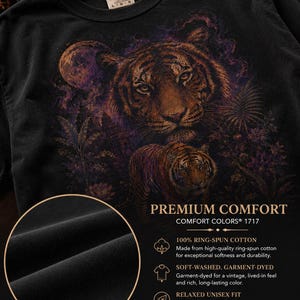 May include: A black t-shirt featuring a graphic print of two tigers in a jungle setting with a moon. The shirt includes text reading PREMIUM COMFORT, COMFORT COLORS 1717, 100% RING-SPUN COTTON, SOFT-WASHED, GARMENT-DYED, RELAXED UNISEX FIT, and BUILT TO LAST.