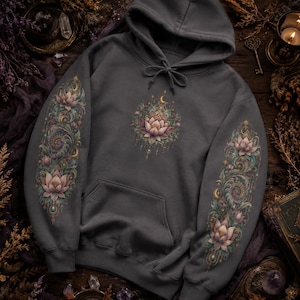 May include: A charcoal gray hooded sweatshirt featuring a central lotus flower graphic on the chest and matching intricate floral and spiral patterns extending down both sleeves. The design incorporates soft pink, teal, and gold accents.