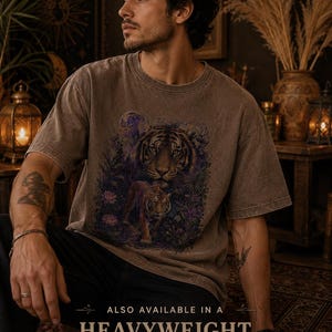 May include: A brown, washed-effect short-sleeve t-shirt featuring a graphic print of two tigers in a jungle setting with a moon. The text at the bottom reads: ALSO AVAILABLE IN A HEAVYWEIGHT, WASHED DROP SHOULDER TEE.