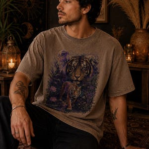 May include: A brown, short-sleeved, crew-neck t-shirt featuring a graphic print of a large tiger face above a smaller tiger walking through a dark, purple-toned forest with foliage and a full moon in the background, rendered in a vintage wash.