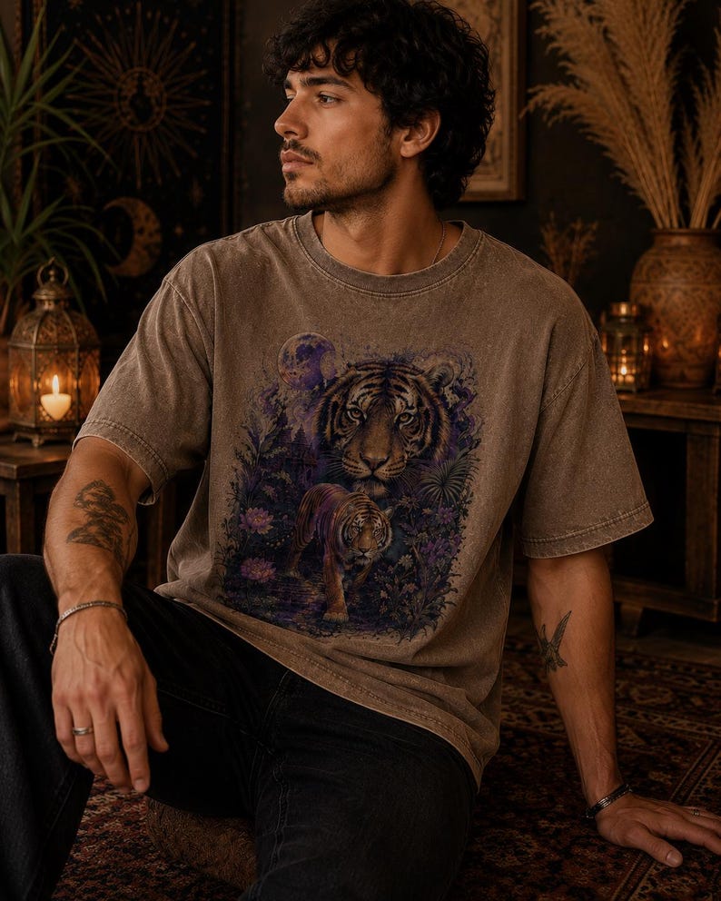 May include: A brown, short-sleeved, crew-neck t-shirt featuring a graphic print of a large tiger face above a smaller tiger walking through a dark, purple-toned forest with foliage and a full moon in the background, rendered in a vintage wash.