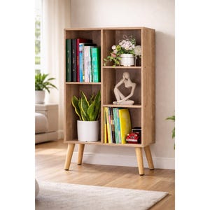 May include: A light brown wooden bookshelf with four shelves and four wooden legs. The shelves contain books, plants, and decorative items. The bookshelf is in a well-lit room with a neutral color palette.