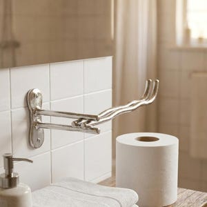 Puede incluir: Escena de baño con un toallero plateado montado en azulejos blancos. Una pila de toallas blancas dobladas, un rollo de papel higiénico y un dispensador de jabón se encuentran en una estantería de madera. La habitación tiene una paleta de colores neutros.