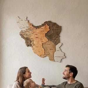 Pode incluir: Um mapa de madeira do Irão, em tons de castanho e bege, está pendurado numa parede. Uma família de três pessoas está sentada num sofá bege, a olhar para o mapa. À esquerda está uma janela grande.