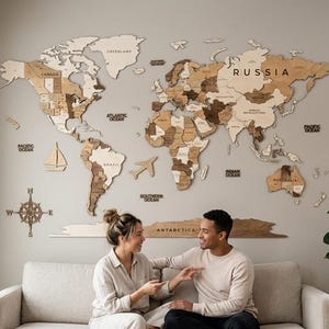 May include: A large wooden world map wall art installation featuring multi-tonal brown laser-cut continents, countries, and oceans. The map includes decorative icons like a compass rose, a sailboat, and an airplane, with text labels for major regions.