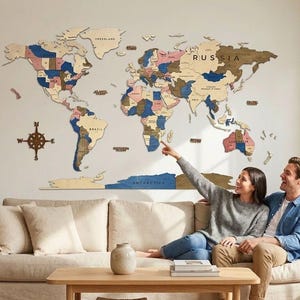 Op de afbeelding: Een grote houten wereldkaart als wanddecoratie met veelkleurige landsegmenten, een windroos en de tekstlabels voor Rusland, Brazilië en Antarctica, gemonteerd op een effen muur boven een beige stoffen bank.