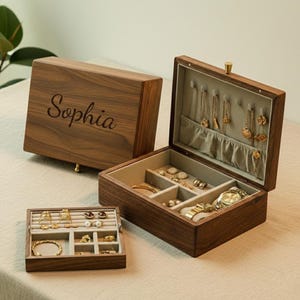 May include: A wooden jewelry box with the name "Sophia" engraved on the lid. The box is open, revealing compartments for jewelry, including necklaces, rings, and a watch. The box is made of dark wood.