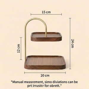 Puede incluir: Un expositor de dos niveles con bandejas cuadradas de madera marr&oacute;n oscuro y un marco de metal dorado. El soporte mide 20 cm de ancho, 15 cm la bandeja superior, 12 cm entre niveles y 24 cm de altura total. Texto abajo: *Manual measrement, simo diviations can be prt irrusttr for obrett.*