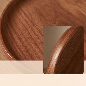 Puede incluir: Una bandeja circular de madera con una superficie lisa y pulida, y un patr&oacute;n de veta de color marr&oacute;n oscuro intenso. La bandeja presenta un borde redondeado ligeramente elevado que se curva hacia adentro, mostrando la textura natural.
