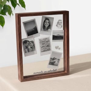 Könnte beinhalten: Ein rechteckiger Holzrahmen mit einer transparenten Glasfront, der mehrere Schwarz-Weiß-Fotos im Polaroid-Stil zeigt. Die Fotos zeigen Landschaften, Paare und Einzelpersonen. Ein Schmetterling und zwei Herzen sind ebenfalls zu sehen. Der Satz "moments we collected" ist unten aufgedruckt.