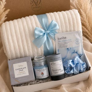 Peut inclure: Un coffret cadeau contenant un plaid blanc c&ocirc;tel&eacute; nou&eacute; avec un ruban bleu clair, une bo&icirc;te de cookies aux p&eacute;pites de chocolat, une bougie parfum&eacute;e cupcake vanille, un masque facial Sadoer Deep Hydration Series, une bo&icirc;te de th&eacute; et un chouchou bleu.