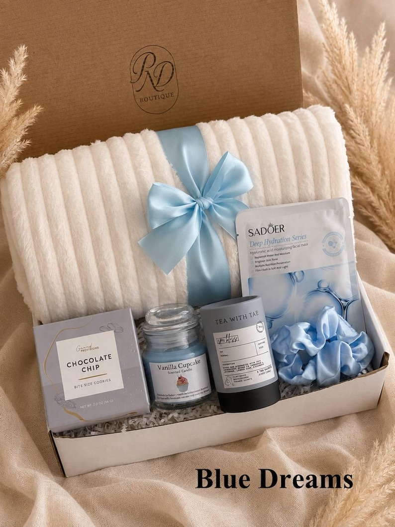 Peut inclure: Un coffret cadeau contenant un plaid blanc c&ocirc;tel&eacute; nou&eacute; avec un ruban bleu clair, une bo&icirc;te de cookies aux p&eacute;pites de chocolat, une bougie parfum&eacute;e cupcake vanille, un masque facial Sadoer Deep Hydration Series, une bo&icirc;te de th&eacute; et un chouchou bleu.