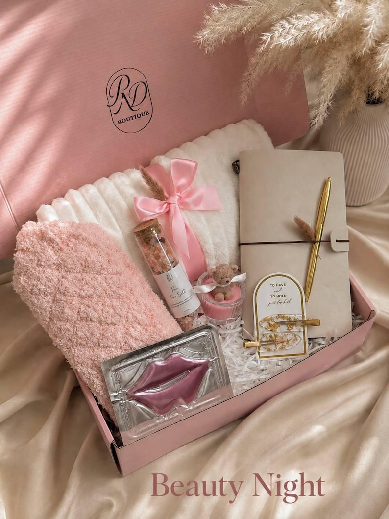 Peut inclure: Une bo&icirc;te cadeau rose contenant une couverture blanche textur&eacute;e nou&eacute;e d'un ruban rose, une paire de chaussettes duveteuses roses, un flacon en verre de sels de bain, une bougie avec un ours, un carnet beige, un stylo dor&eacute; et deux pinces &agrave; cheveux.