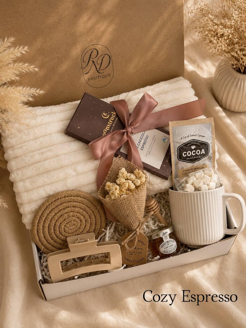 Peut inclure: Un coffret cadeau contenant un plaid blanc c&ocirc;tel&eacute;, une tablette de chocolat noir avec un ruban mauve, un sachet de cacao saveur vanille fran&ccedil;aise, une tasse blanche c&ocirc;tel&eacute;e, un petit pot de miel, une cuill&egrave;re &agrave; miel en bois, une pince &agrave; cheveux beige et des fleurs s&eacute;ch&eacute;es.