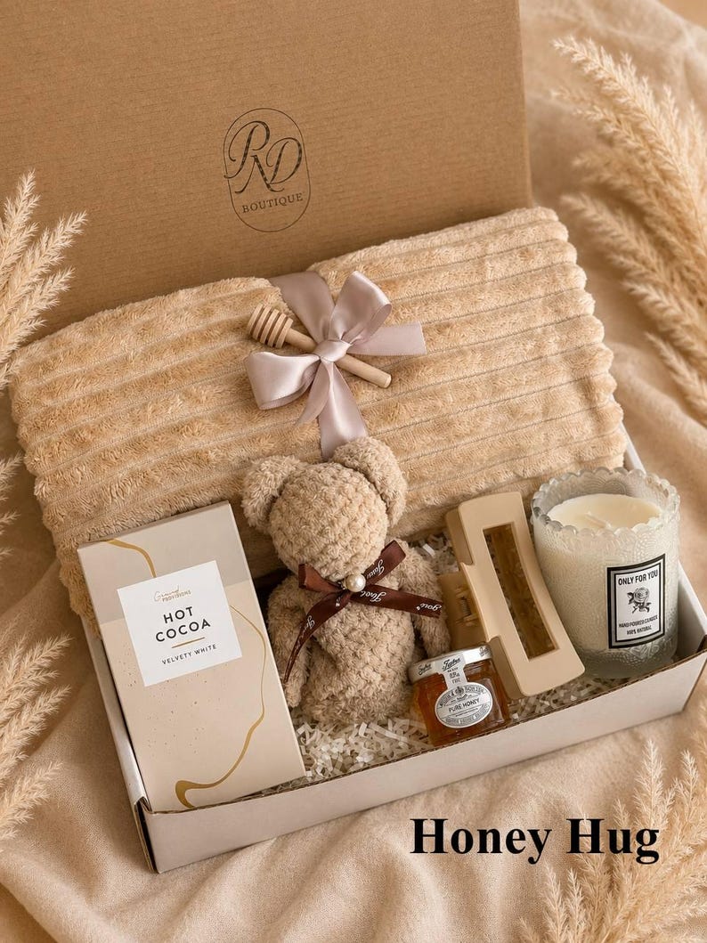 Peut inclure: Un coffret cadeau contenant une couverture beige c&ocirc;tel&eacute;e nou&eacute;e avec un ruban et un b&acirc;ton &agrave; miel en bois, un ours en peluche, une bo&icirc;te de Hot Cocoa Velvety White, une pince &agrave; cheveux beige, un petit pot de miel et une bougie Only For You.