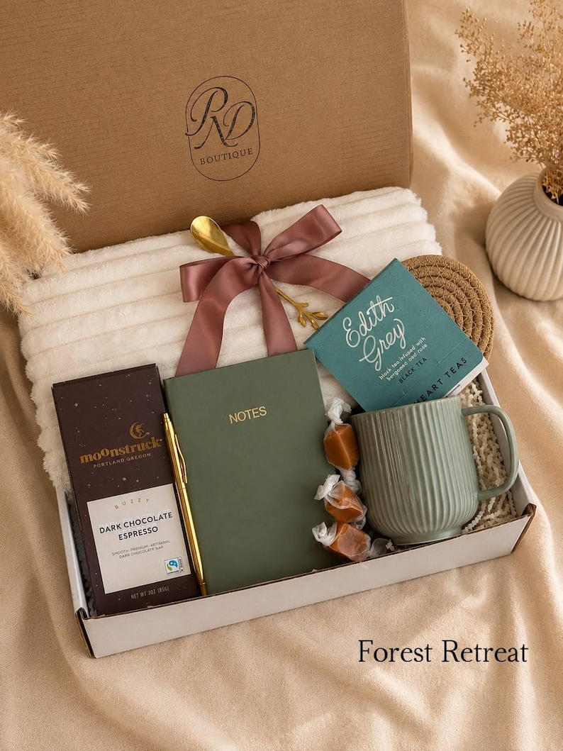 Peut inclure: Un coffret cadeau contenant une couverture blanche c&ocirc;tel&eacute;e avec un ruban mauve, une tablette de chocolat noir espresso Moonstruck, un carnet vert &eacute;tiquet&eacute; NOTES, un stylo dor&eacute;, une bo&icirc;te de th&eacute; Edith Grey, une tasse vert sauge et trois caramels.
