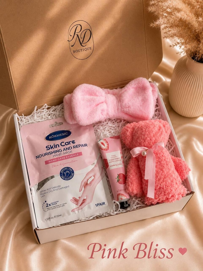 May include: A pink gift box containing a pink headband, a hand mask, a strawberry hand cream, and a pink teddy bear. The box is labeled "RD Boutique" and the text "Pink Bliss" is at the bottom.