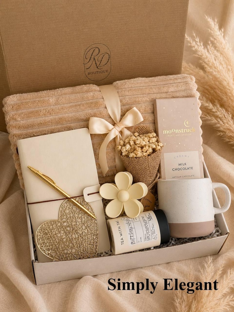 Peut inclure: Un coffret cadeau contenant une couverture c&ocirc;tel&eacute;e beige avec un ruban en satin, un carnet cr&egrave;me avec un stylo dor&eacute;, un ornement en fil dor&eacute; en forme de c&oelig;ur, un petit bouquet de fleurs s&eacute;ch&eacute;es, une pince &agrave; cheveux fleur, une bo&icirc;te de th&eacute; et du chocolat.