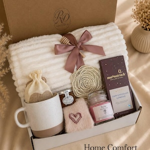 Peut inclure: Un coffret cadeau contenant un plaid blanc c&ocirc;tel&eacute; nou&eacute; avec un ruban mauve et une cuill&egrave;re &agrave; miel en bois, une tasse en c&eacute;ramique mouchet&eacute;e, un petit pot de miel, un dessous de verre dor&eacute;, une bougie rose, une pochette brod&eacute;e et du chocolat noir.