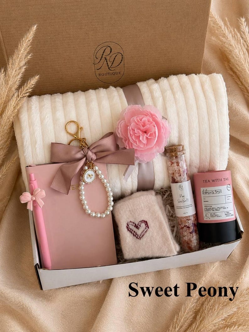 Peut inclure: Un coffret cadeau contenant un plaid c&ocirc;tel&eacute; cr&egrave;me, un carnet rose avec un stylo assorti, un porte-cl&eacute;s en perles avec un n&oelig;ud rose, une fleur en tissu rose, des chaussettes beiges avec un c&oelig;ur, du sel marin en tube et du th&eacute;.