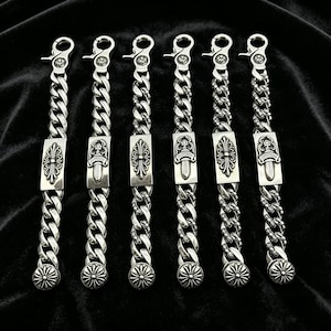 Peut inclure: Six bracelets en chaîne argentés avec des pièces centrales rectangulaires ornées et des embouts décoratifs. Chaque bracelet est composé d'une grosse chaîne gourmette et d'un fermoir mousqueton. Les pièces centrales ont un motif floral et un poignard.