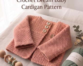 Könnte beinhalten: Eine pfirsichfarbene gehäkelte Babyjacke mit strukturiertem Maschenbild, drei runden Strassknöpfen und einem kleinen braunen Etikett. Der Text lautet Crochet Dream Baby Cardigan Pattern und Instant PDF Download.