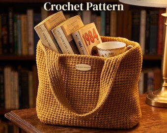 Könnte beinhalten: Eine senfgelbe Häkeltasche mit strukturiertem Schlingenmuster und einem kleinen ovalen Etikett mit der Aufschrift Elara Knits. Die Tasche enthält drei Bücher mit den Titeln Pride & Prejudice, Jane Eyre und 1984 sowie eine geblümte Teetasse. Der Text lautet Fluffy Loop Market Bag Crochet Pattern und Instant PDF Download.