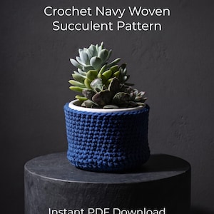 May include: A navy blue crochet plant pot cover featuring a textured woven stitch pattern. The cover holds a white ceramic pot containing a cluster of green and grey-toned succulent plants. The text reads: Crochet Navy Woven Succulent Pattern Instant PDF Download.