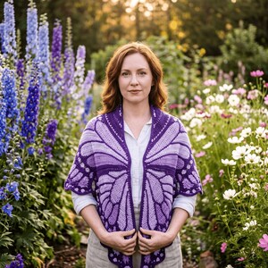 Puede incluir: Un chal de ganchillo con un patr&oacute;n de alas de mariposa en tonos morado y lavanda. La prenda tiene un borde festoneado y se lleva sobre una camisa blanca de cuello y pantalones claros, mostrando un trabajo de tejido detallado y texturas.